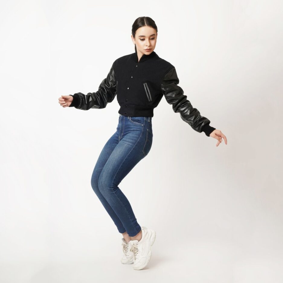 A stylish black wool and leather letterman crop top jacket with rib knit collar and cuffs, featuring snap button closure and two open hem side pockets.
